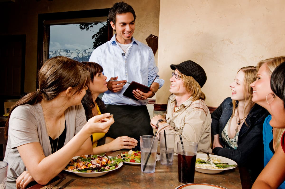 Camarero atendiendo con una sonrisa a varios clientes de un restaurante