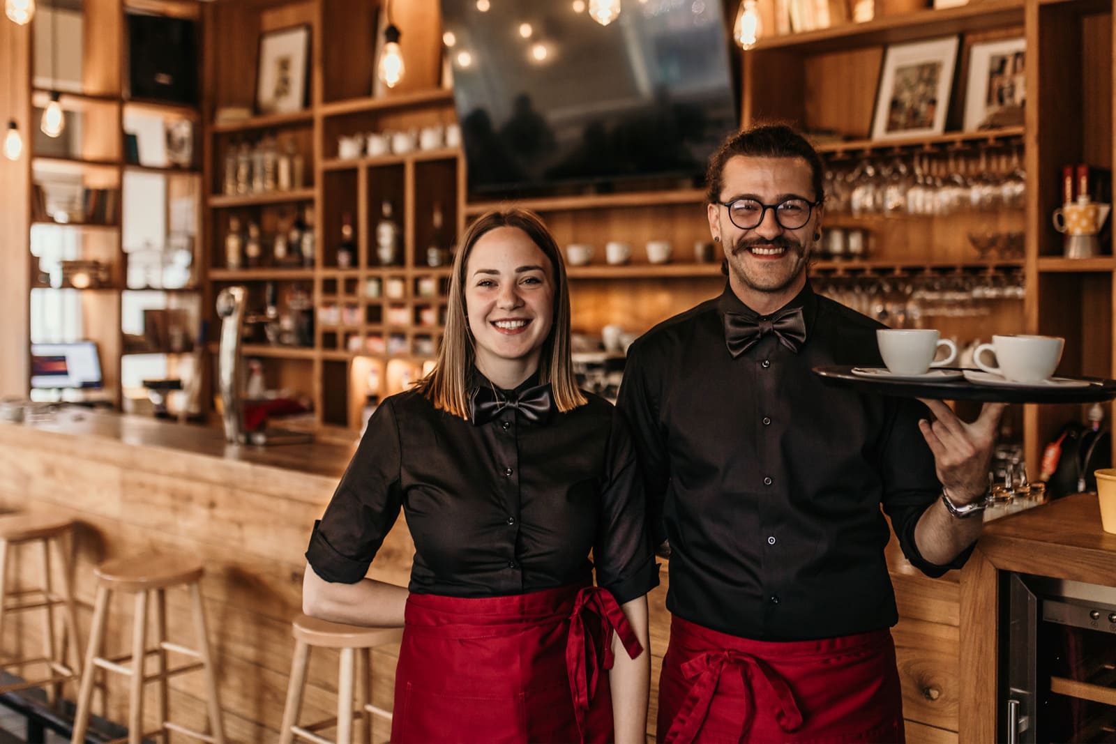 Dos camareros sonrientes posando en el interior del restaurante y llevando una bandeja con dos tazas