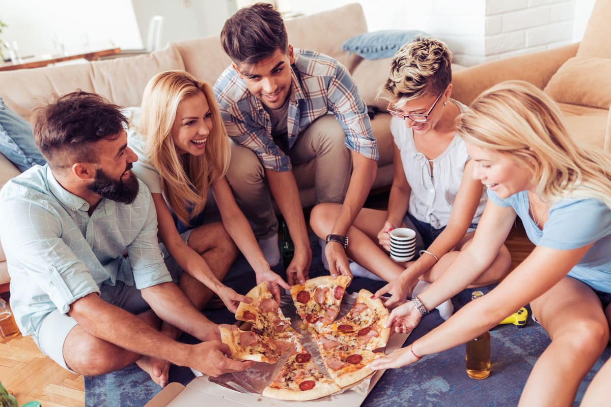 Grupo de amigos comiendo pizza en casa que han pedido a domicilio