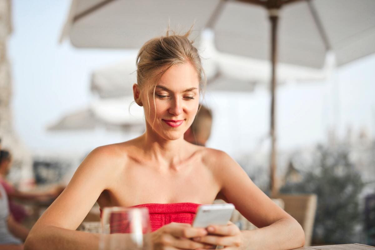 Chica sentada en una terraza usando su teléfono móvil para pagar la cuenta del restaurante