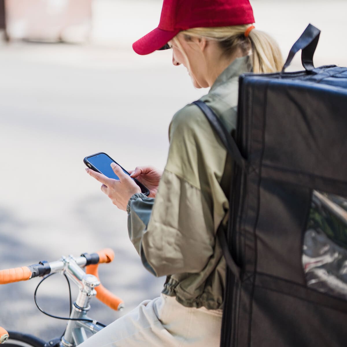 Chica repartidora de comida a domicilio subida en la bici y comprobando la dirección de reparto en su smartphone