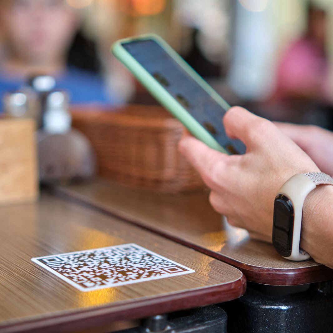 Persona sentada en la mesa de un restaurante escaneando un código QR para poder acceder el menú online
