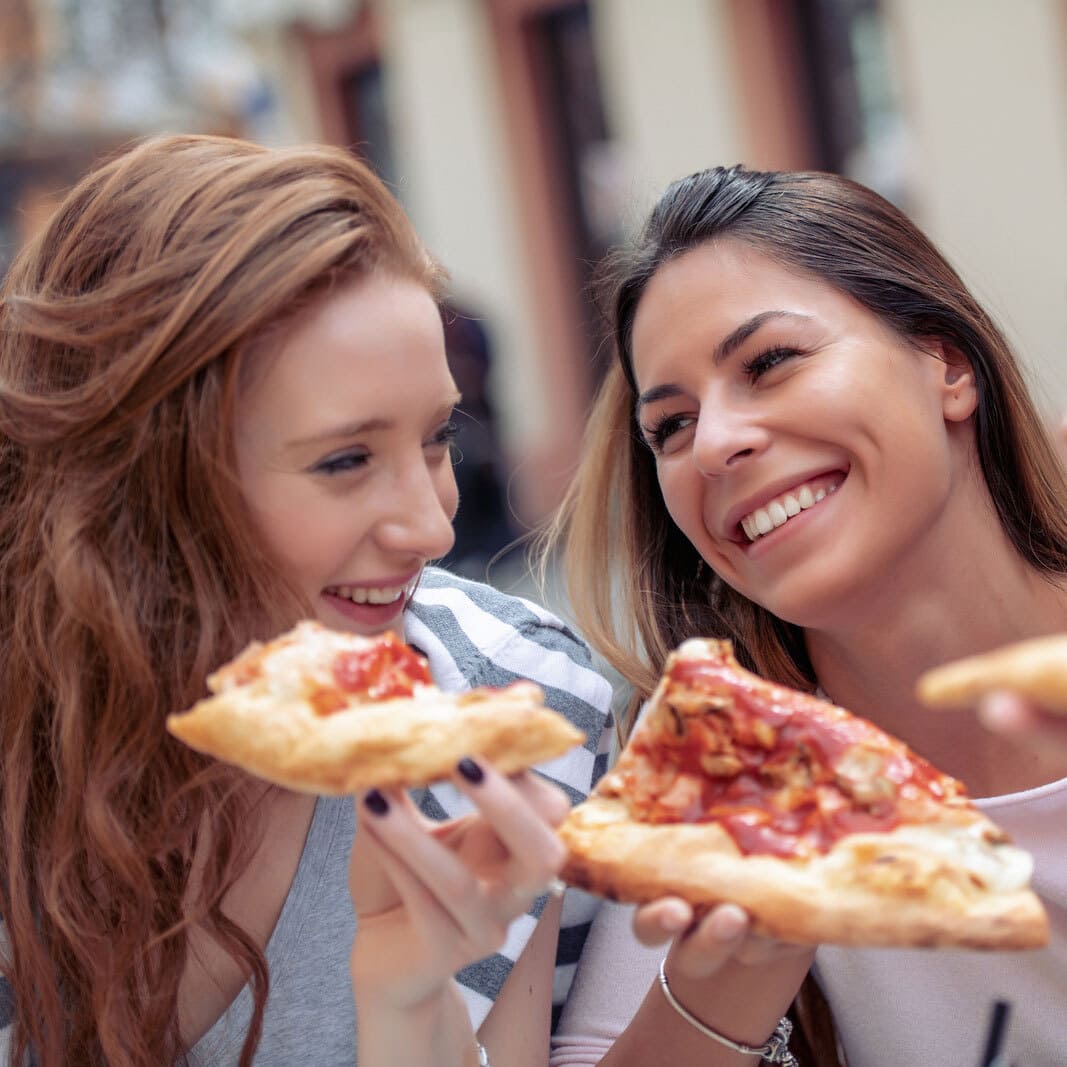 Tres chicas felices sonriendo y comiendo pizza