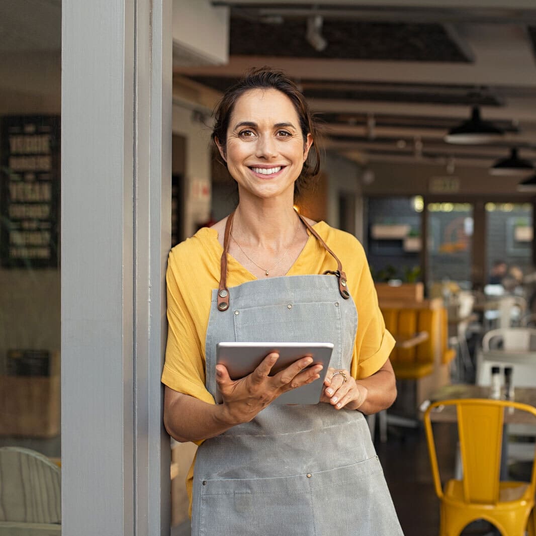 Camarera sonriendo en la puerta del restaurante sosteniendo un tablet para hacer las comandas de los clientes
